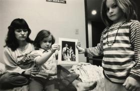 Mary & her daughters holding a family portrait with their father, Minneapolis, 1987